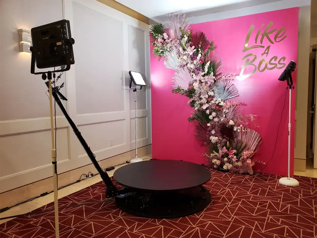 Indoor 360 video booth setup with a pink floral backdrop reading 'Like A Boss.' Equipped with professional lighting and an automatic camera arm for high-quality event photography