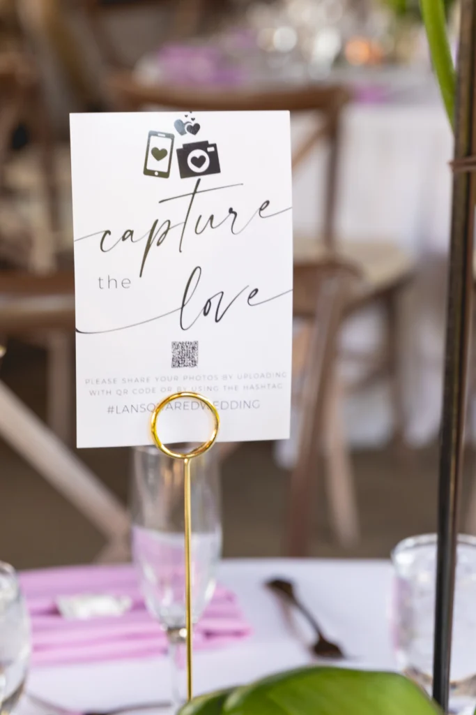 Wedding table card with 'Capture the Love' message, inviting guests to share photos via QR code or hashtag.