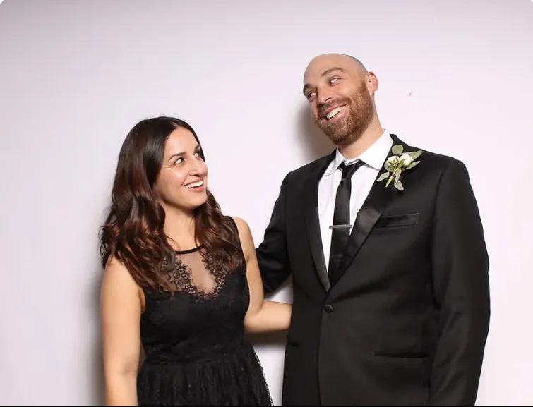 Smiling couple posing in front of a white photo booth backdrop at a wedding.