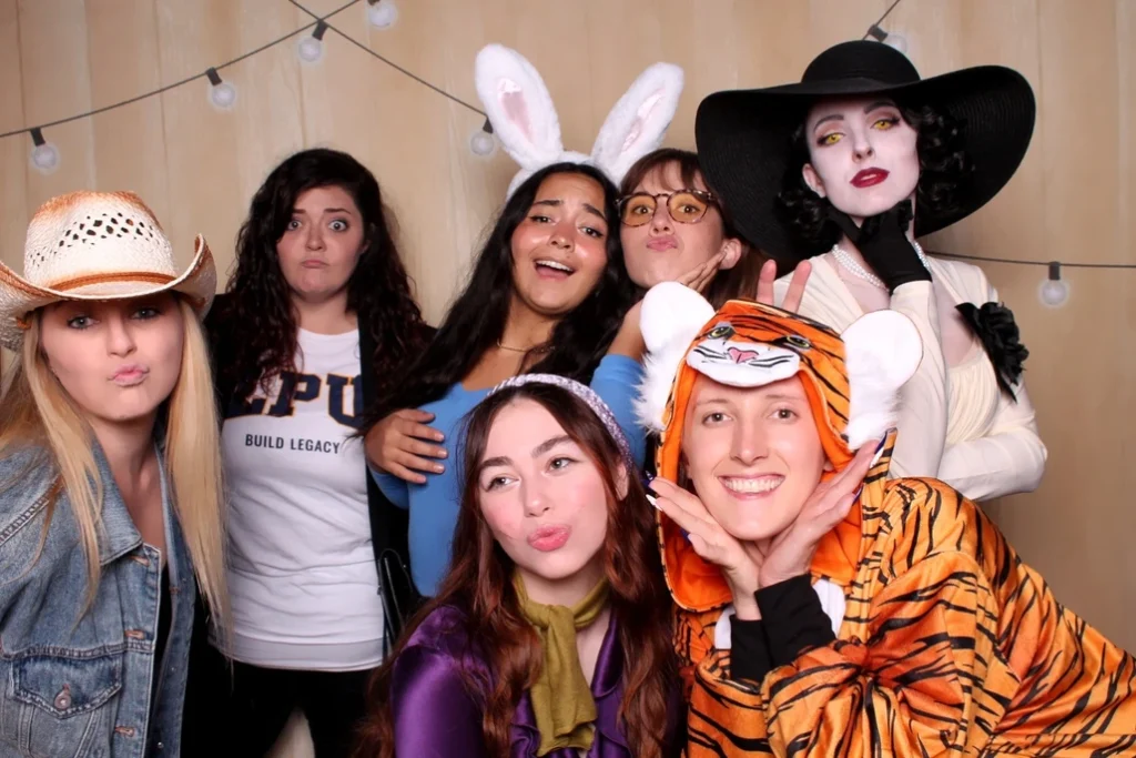 Group of friends in creative costumes posing in a fun fall festival photo booth.