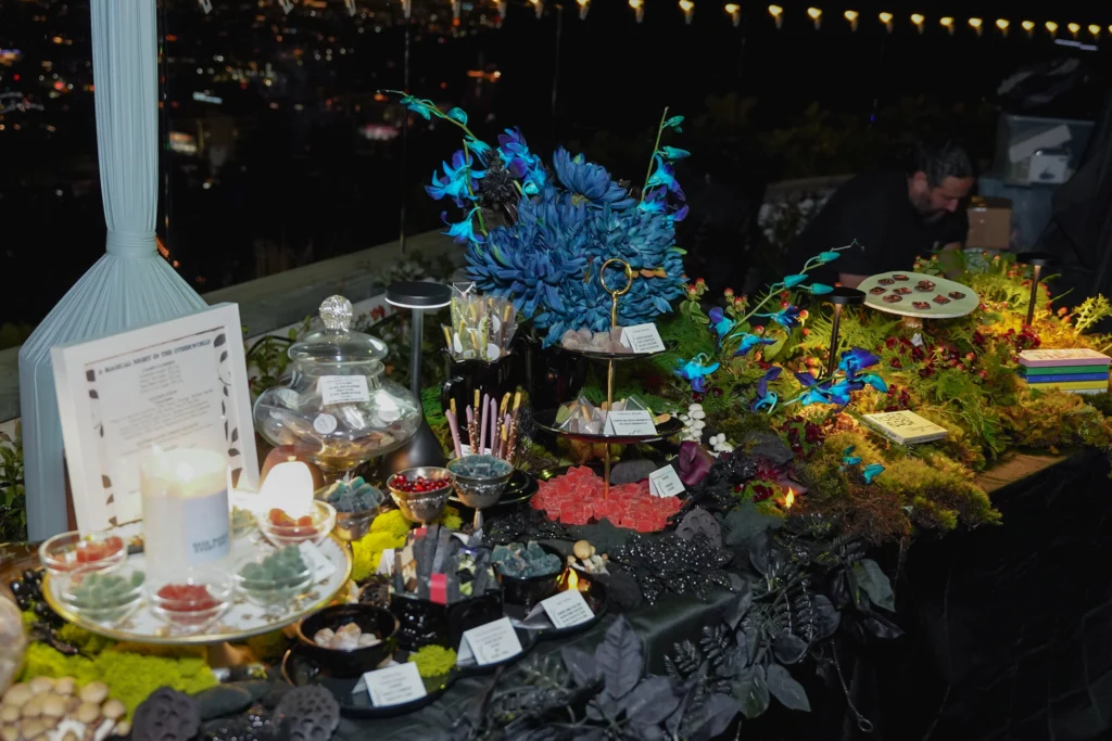 Magical themed dessert table with vibrant blue flowers, decorative lights, and assorted sweets displayed elegantly.