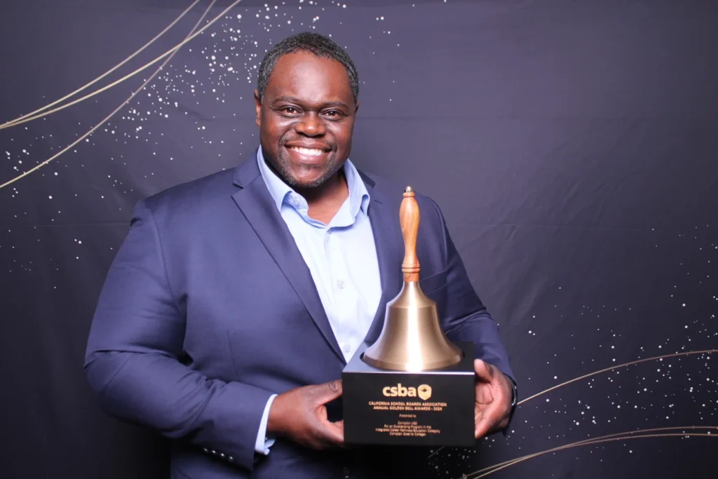 Man smiling and holding an award trophy at a corporate awards ceremony.