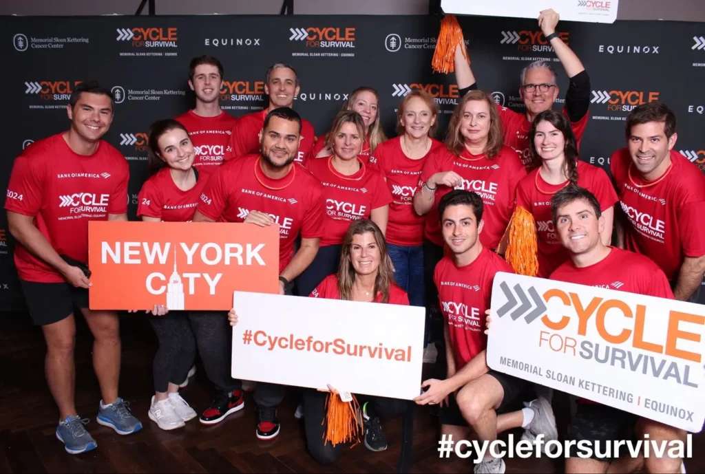 Team posing in red shirts at a Cycle for Survival charity event with signs and smiles.