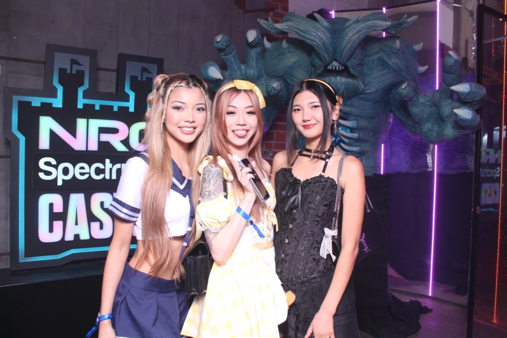 Three women posing at a themed corporate event with a fantasy creature backdrop.