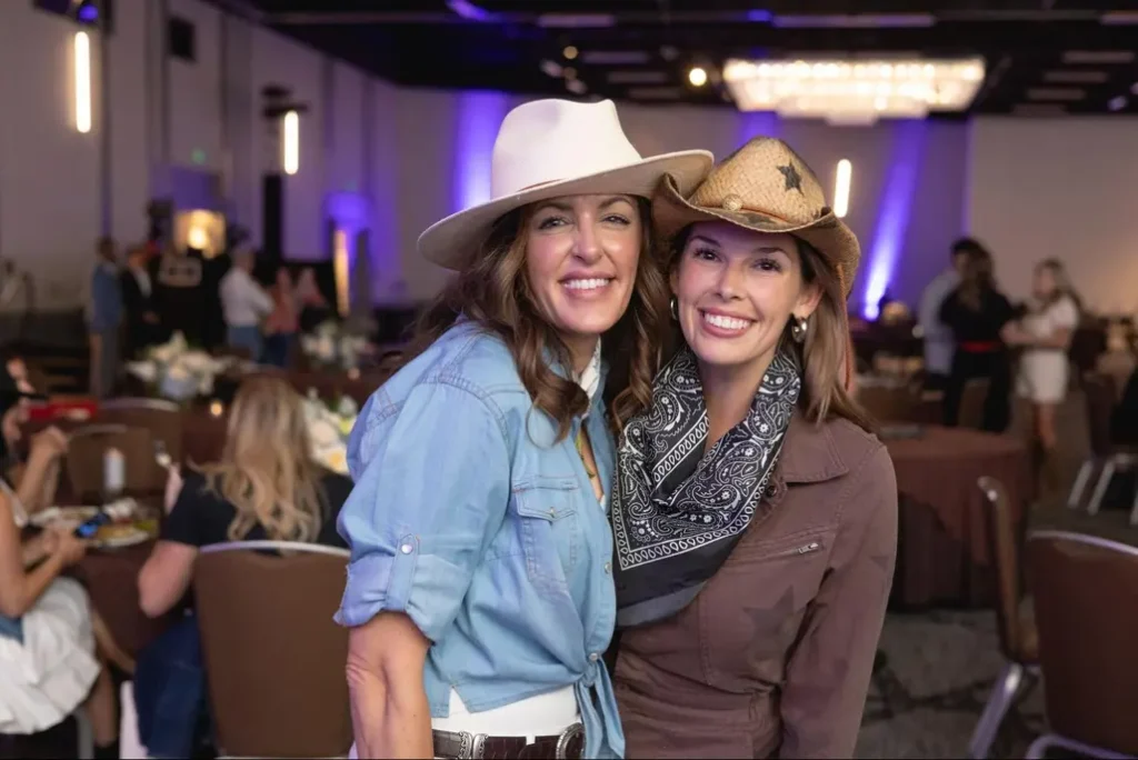 Two women in cowboy hats smiling at a rustic-themed fall festival event.