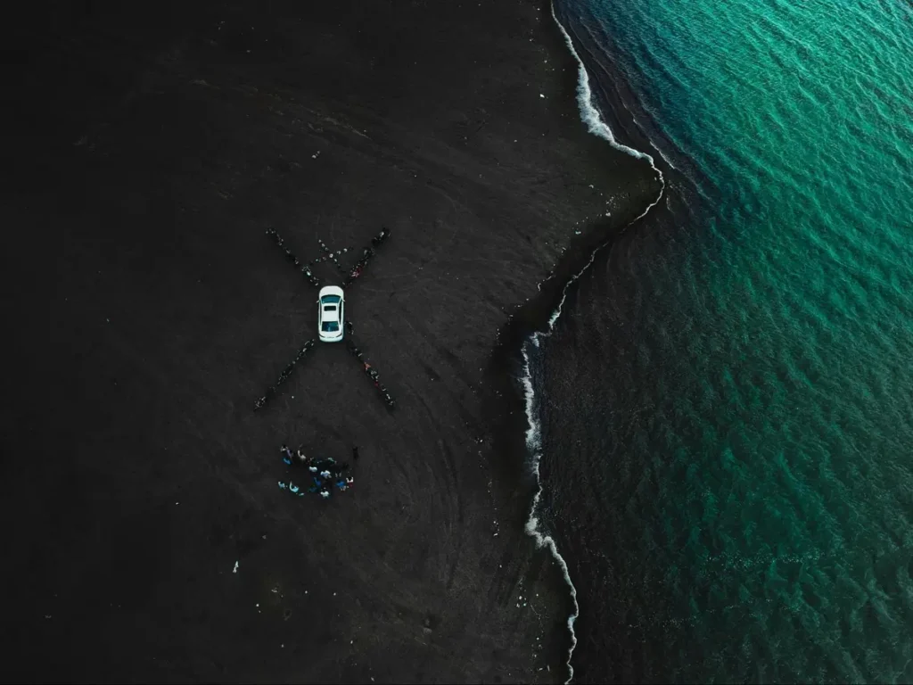 Aerial drone photography of car on black sand beach with turquoise ocean, showcasing innovative perspective in landscape shots