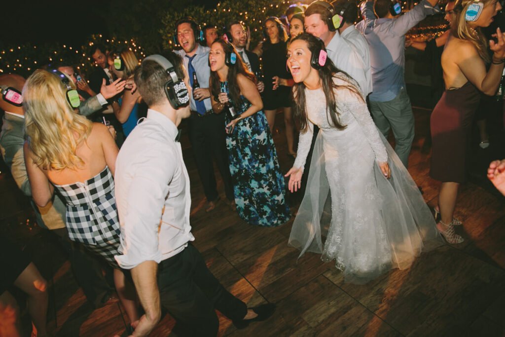 Bride and wedding guests dancing joyfully at outdoor silent disco reception with colorful LED headphones