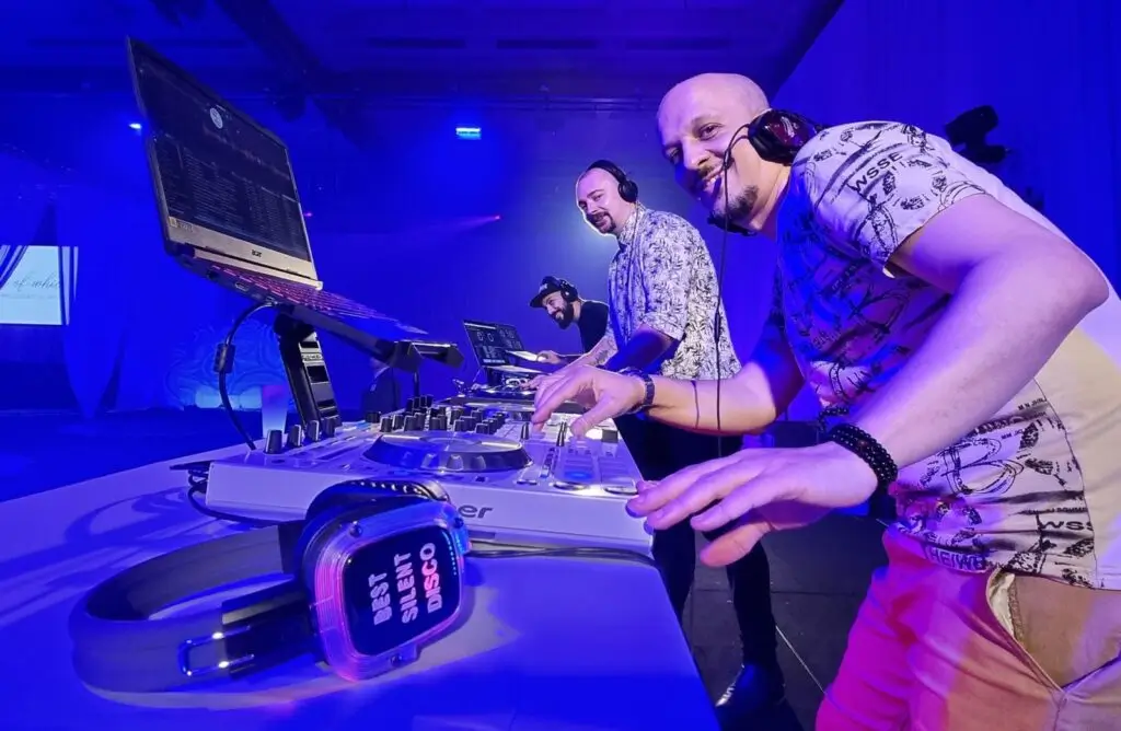 DJs operating Pioneer equipment at silent disco event, bathed in blue lighting while wearing wireless headphones