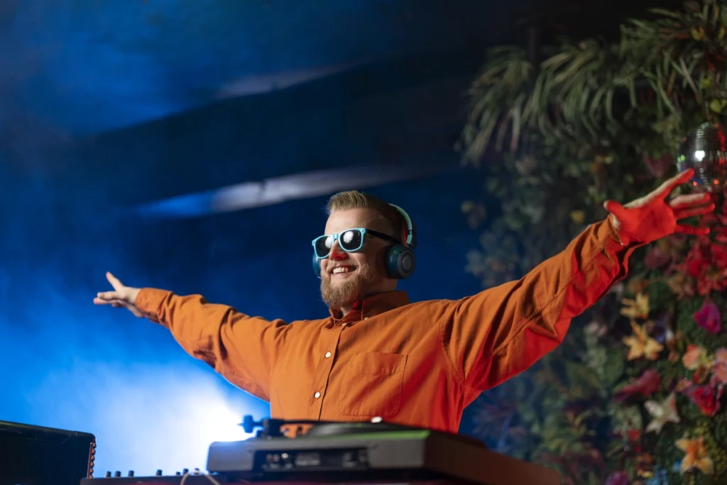 Energetic DJ wearing sunglasses and wireless headphones spreads arms wide while performing at outdoor silent disco