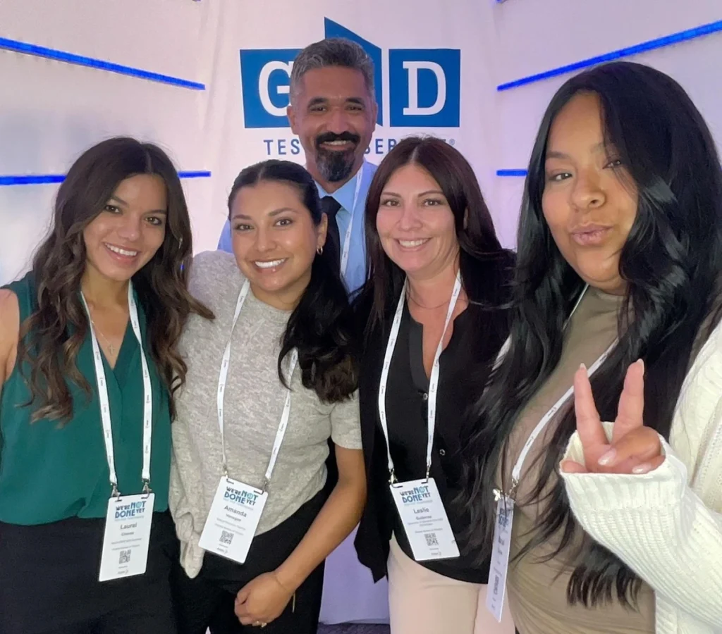 Group photo of conference attendees at GD Testimonials booth, showing diverse team members with name badges and company branding