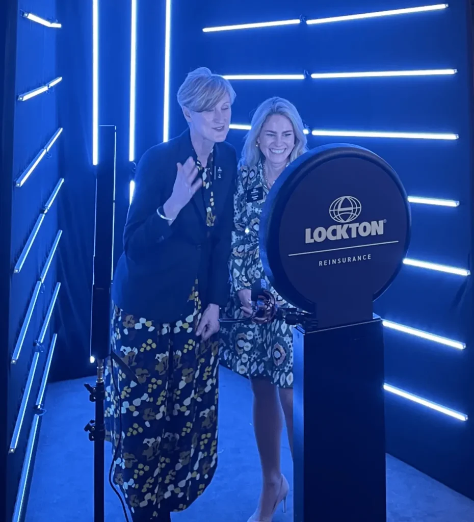 Two attendees laughing during Lockton insurance corporate video shoot with blue neon lighting and Lockton Reinsurance branding