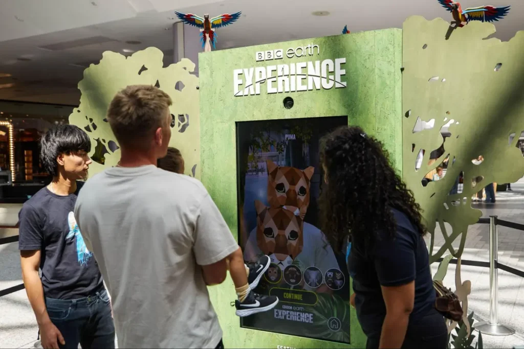 BBC Earth Experience interactive display booth with colorful parrot decorations where visitors engage with a digital puma animation on screen