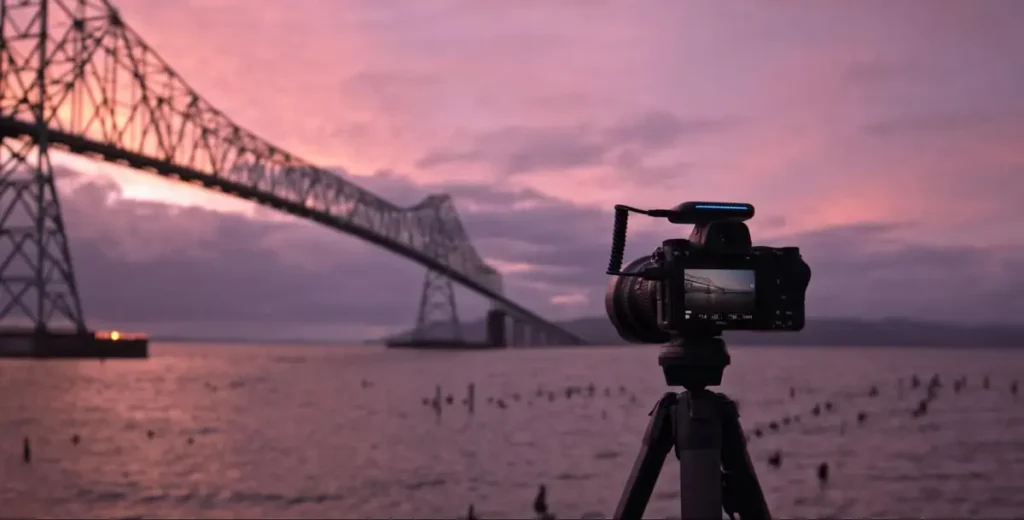 Camera on tripod capturing sunset view of a bridge over water, demonstrating professional event photography setup