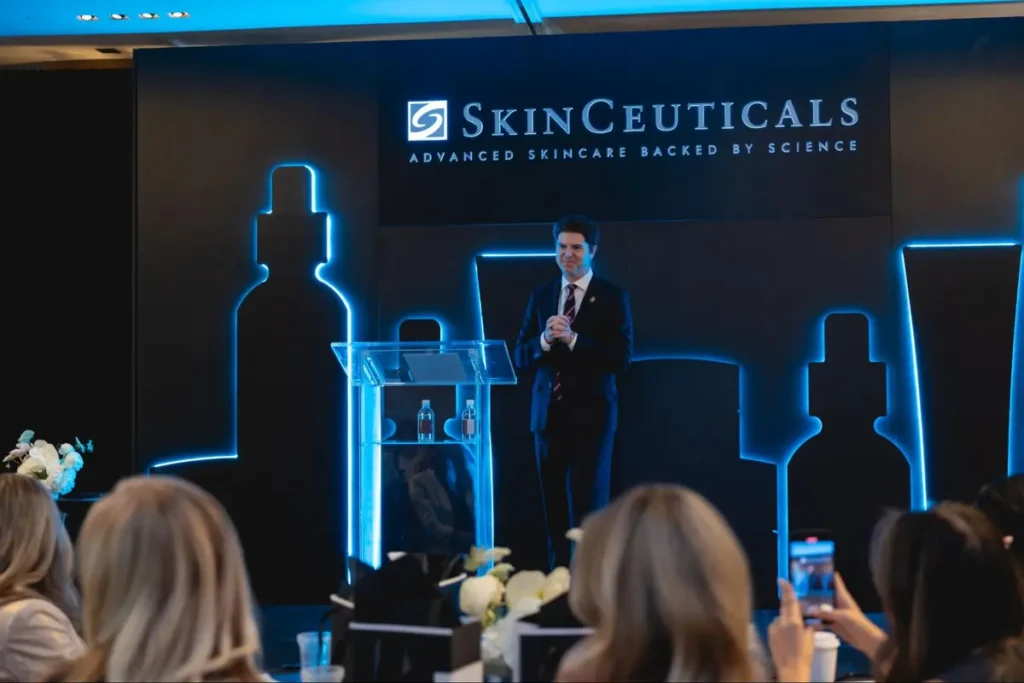 Corporate product launch event for SkinCeuticals skincare with presenter on stage featuring blue-lit product silhouettes