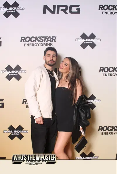 Couple at branded photo wall with multiple sponsor logos including Rockstar Energy, NRG, and FullSquad Gaming at Who's The Imposter event