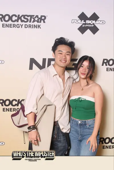 Couple posing in front of branded step-and-repeat backdrop featuring Rockstar Energy, NRG, and FullSquad Gaming logos at Who's The Imposter premiere