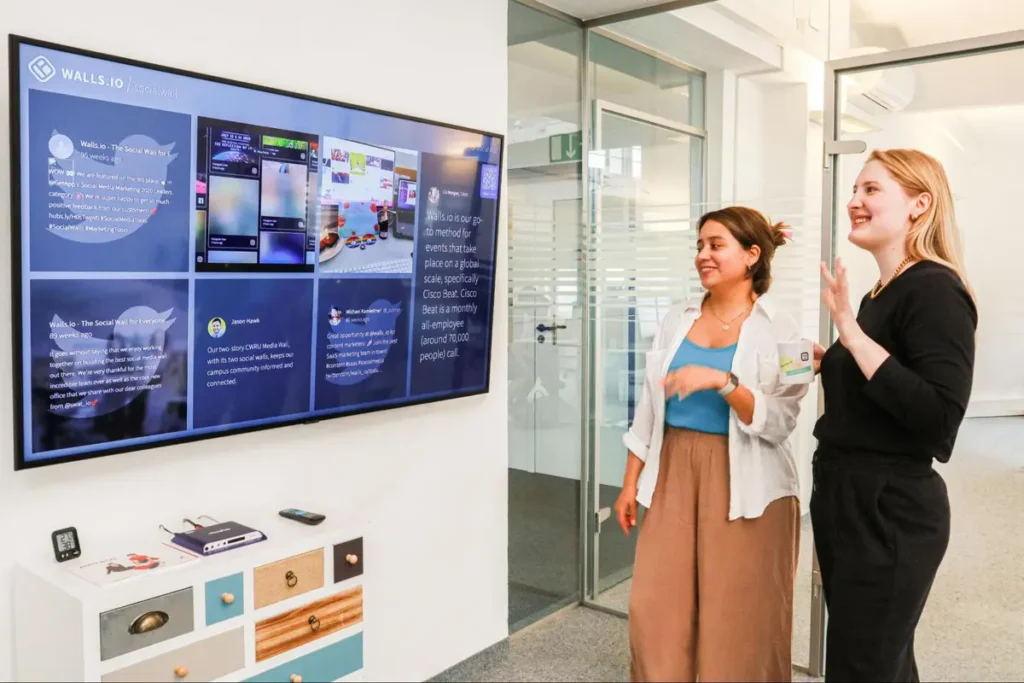 Employees engaging with WALLS.IO social wall display in modern office space, showcasing digital content sharing at corporate events