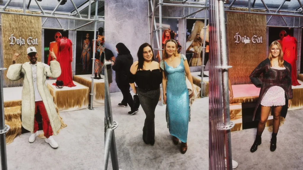 Fashion showroom with Duja Cat branding displaying clothing items on furry pedestals with attendees viewing the exhibition