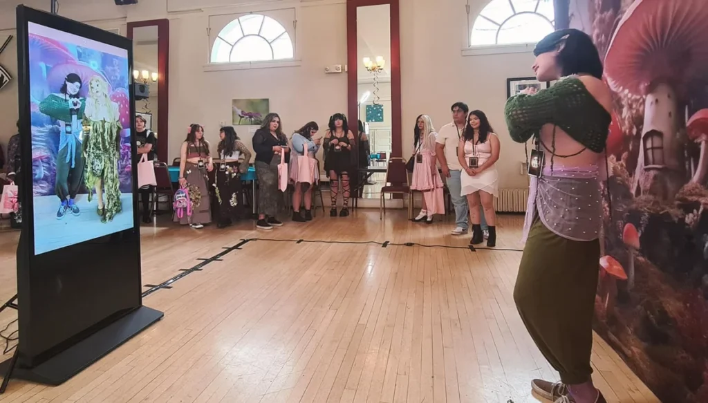 Interactive digital display at an event showing virtual avatars, with attendees in themed costumes gathering to view their digital representations