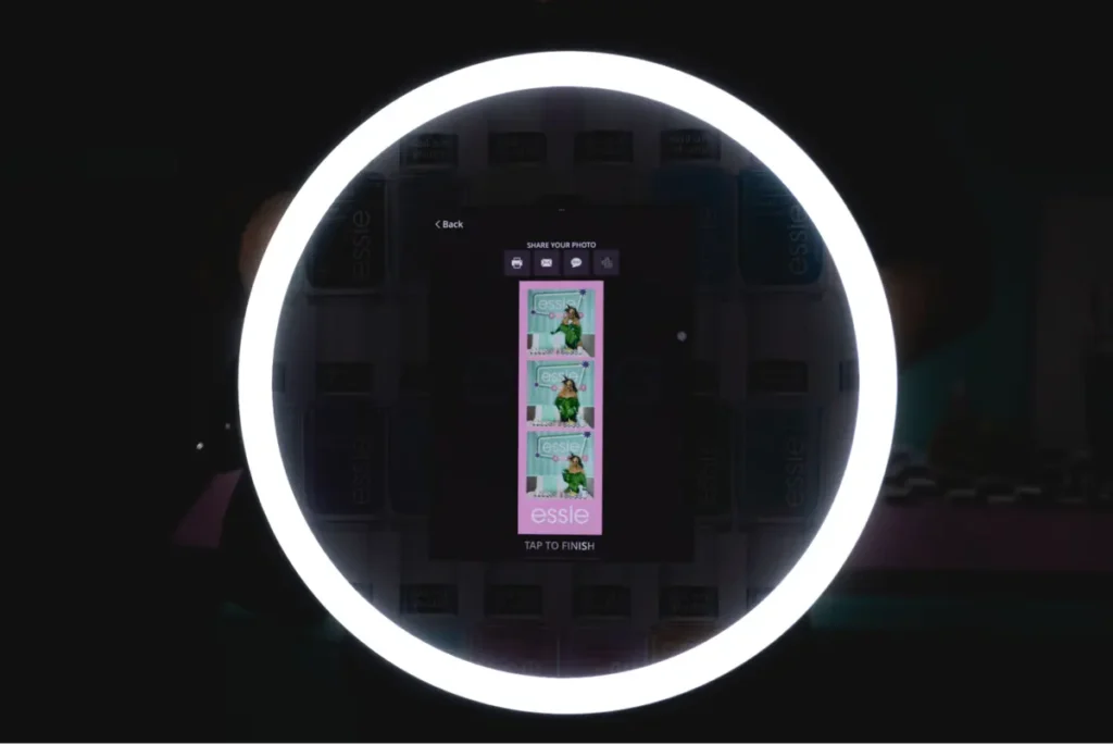 Interactive photo booth display showing Essie branded photo strip with sharing options and ring light, encouraging brand engagement