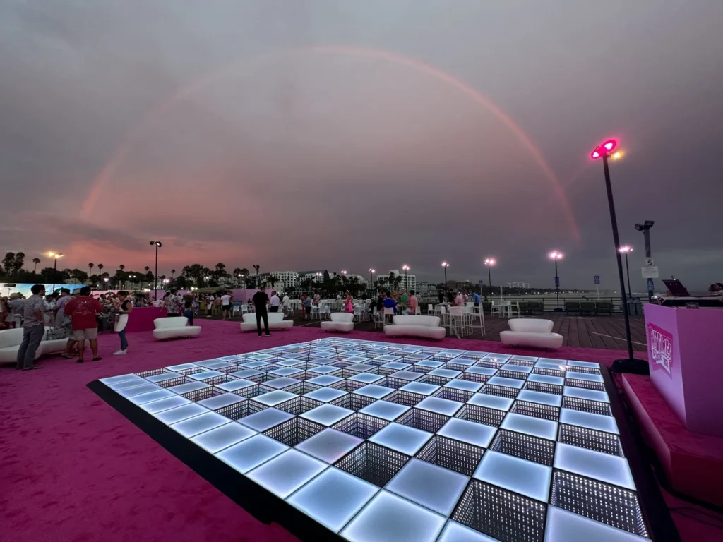 Outdoor corporate event with LED dance floor under a rainbow, featuring lounge seating and waterfront views for memorable entertainment