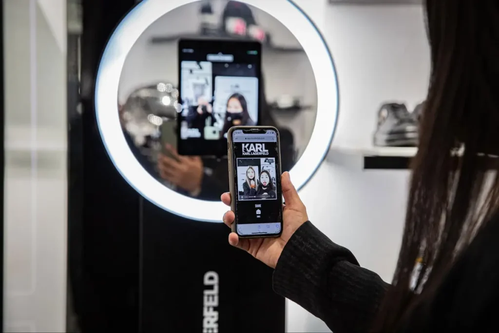 Person taking selfie with smartphone at a Karl Lagerfeld branded photo booth with ring light, demonstrating interactive retail experience