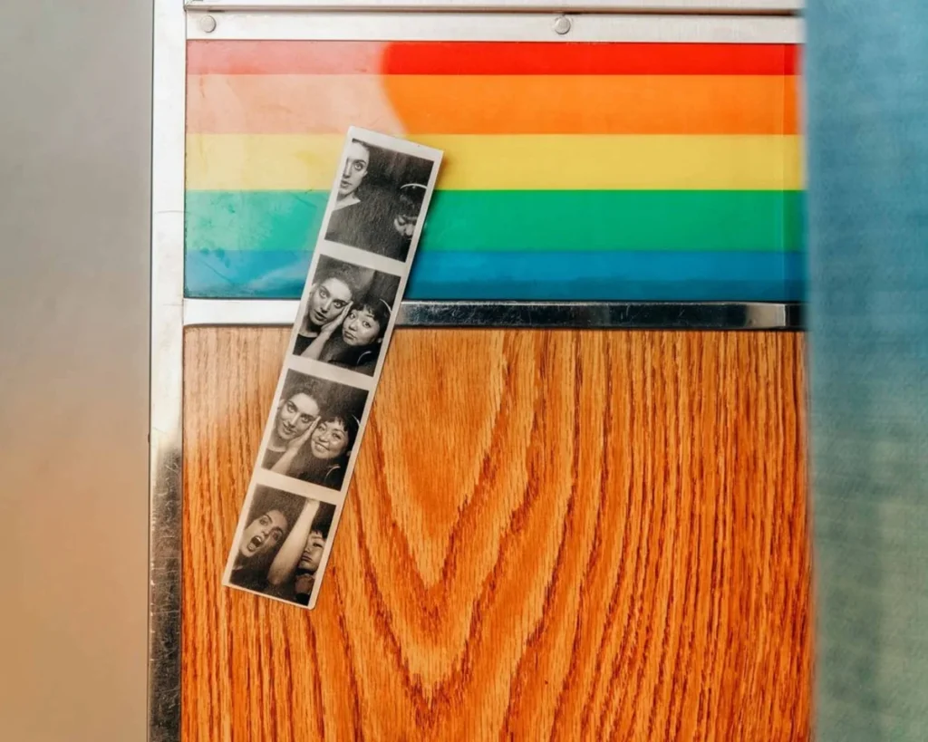 Photo strip with four fun poses displayed against a rainbow pride flag background and wooden surface