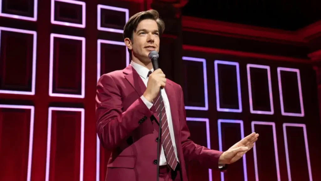 Professional comedian in a burgundy suit performing stand-up comedy at a corporate event, engaging the audience with microphone in hand