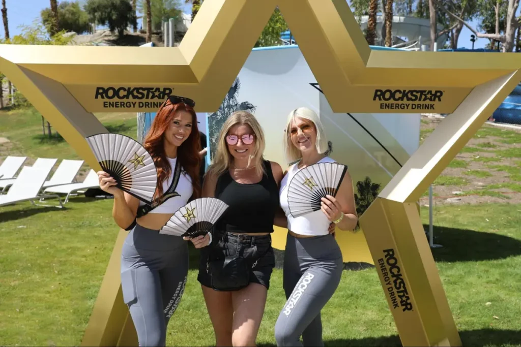 Rockstar Energy Drink promotional booth with brand ambassadors holding fans at outdoor event