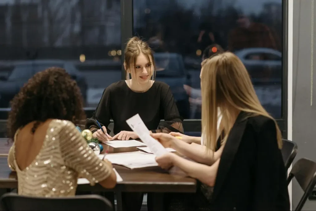 Three women in business attire reviewing event documents during evening planning session