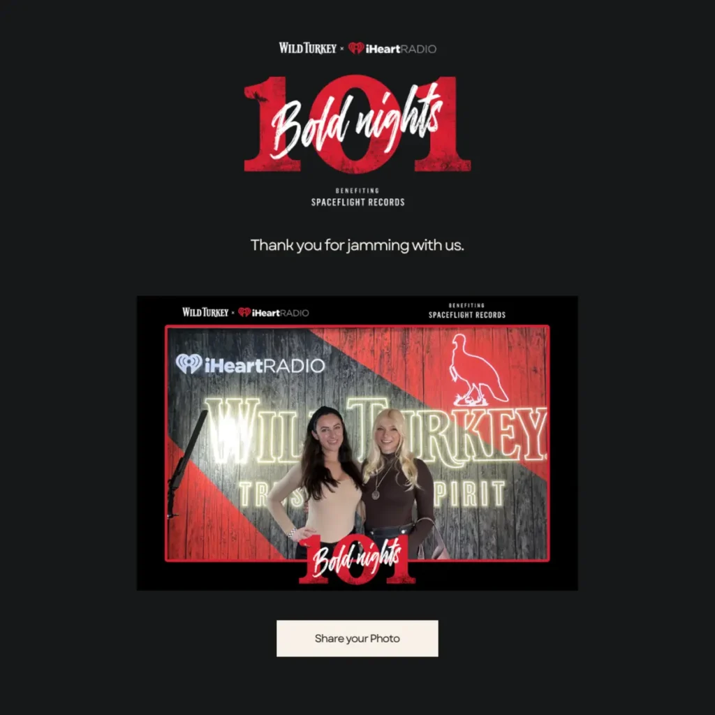 Wild Turkey and iHeartRadio's Bold Nights 101 event branded photo booth with two attendees posing against custom branded backdrop