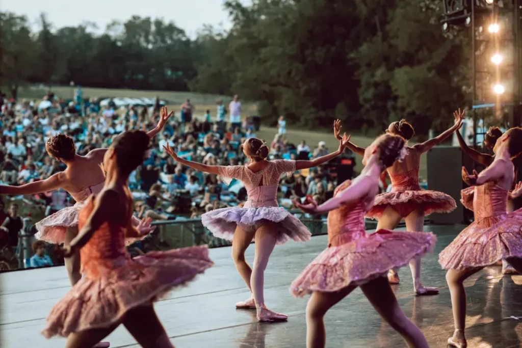 Ballet dancers in pink tutus performing on outdoor stage with audience, perfect for arts festival or cultural event themes
