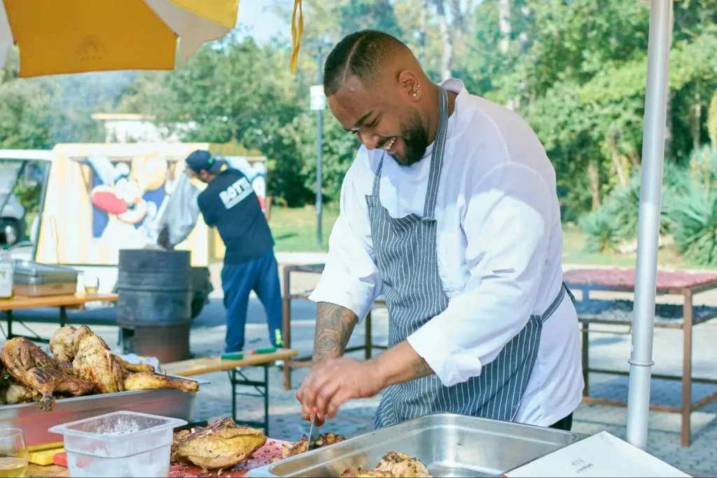 Chef in white uniform and striped apron preparing barbecue at outdoor food festival - Culinary event with live cooking demonstrations