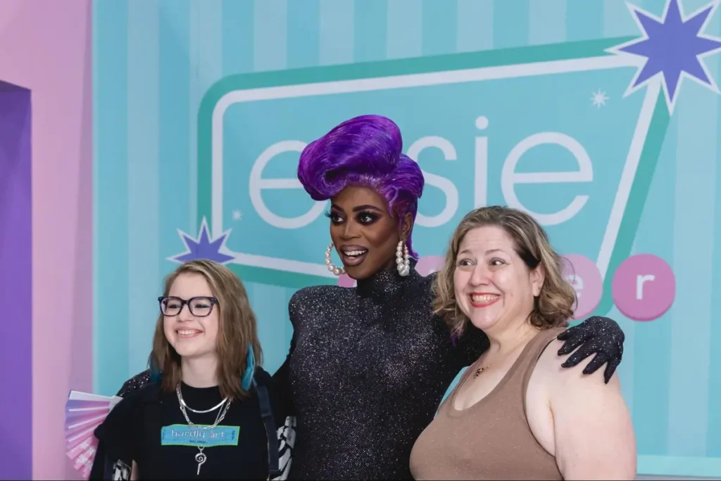 Drag performance event featuring performer in purple wig with attendees at Essie-sponsored venue