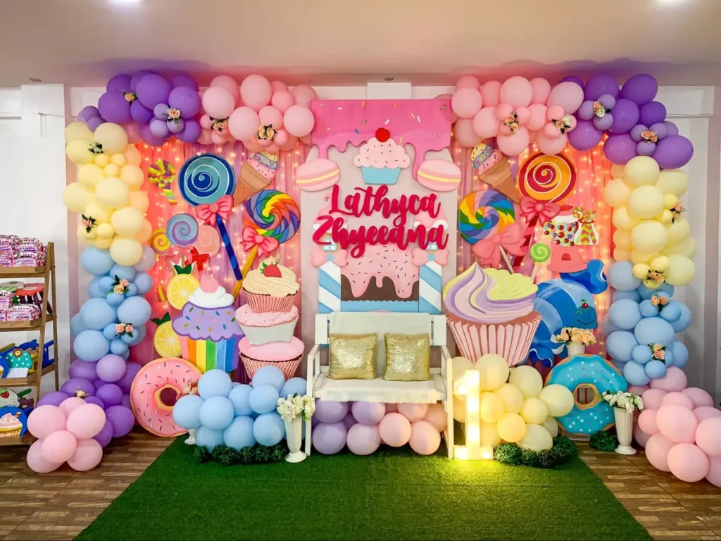 Elaborate candy-themed birthday celebration with balloon arrangements, cupcake decorations and customized backdrop for Lathyca Zhyeana