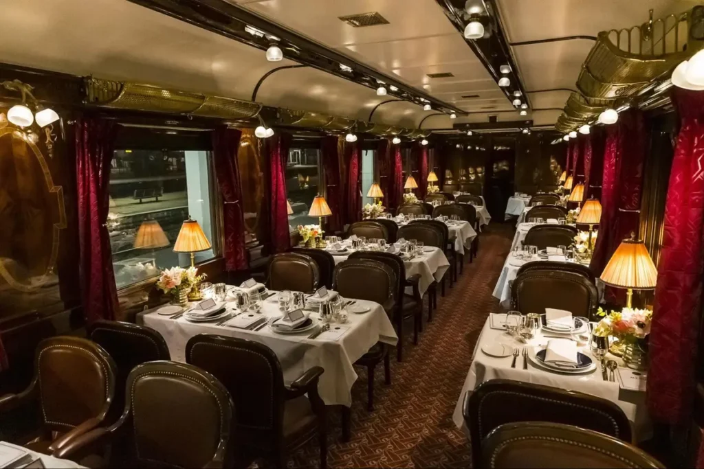 Elegant luxury dining car interior with white tablecloths, red curtains and warm lighting - vintage train travel themed event
