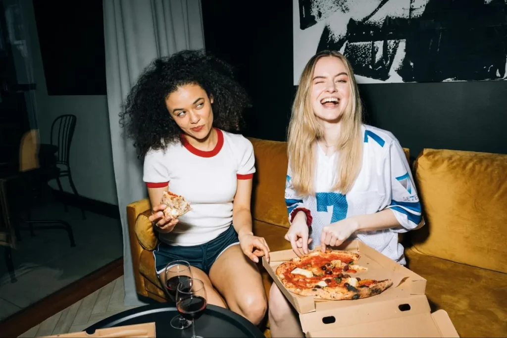 Friends enjoying pizza night on yellow couch, perfect for casual home entertainment or comfort food themed gatherings