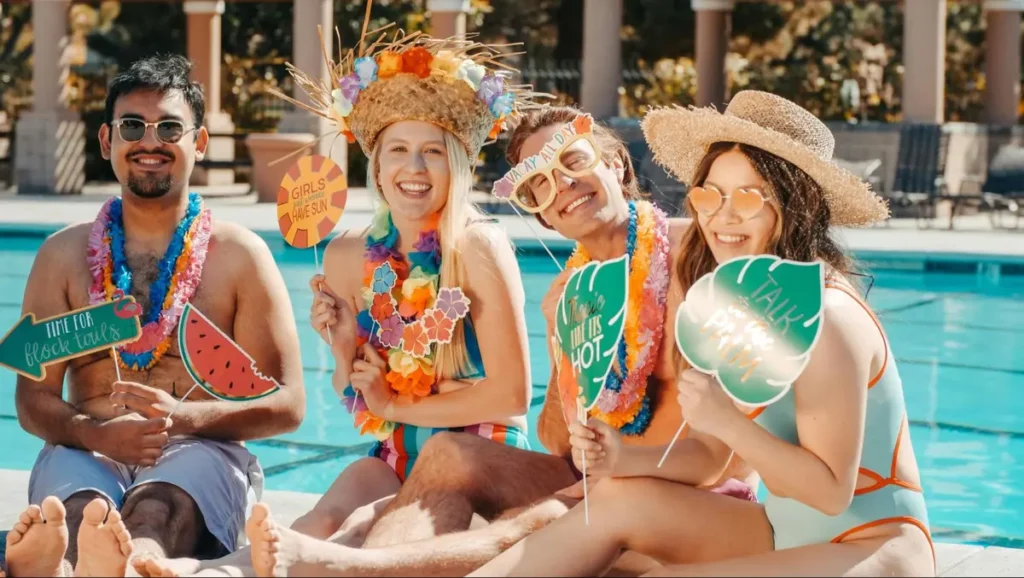 Group of friends enjoying a tropical pool party with Hawaiian leis, decorative props, and festive summer accessories