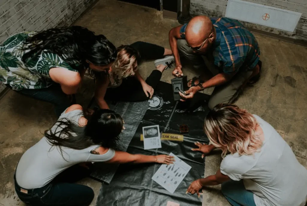 Group of people gathered around a mystery-themed escape room challenge with clues and cryptic materials