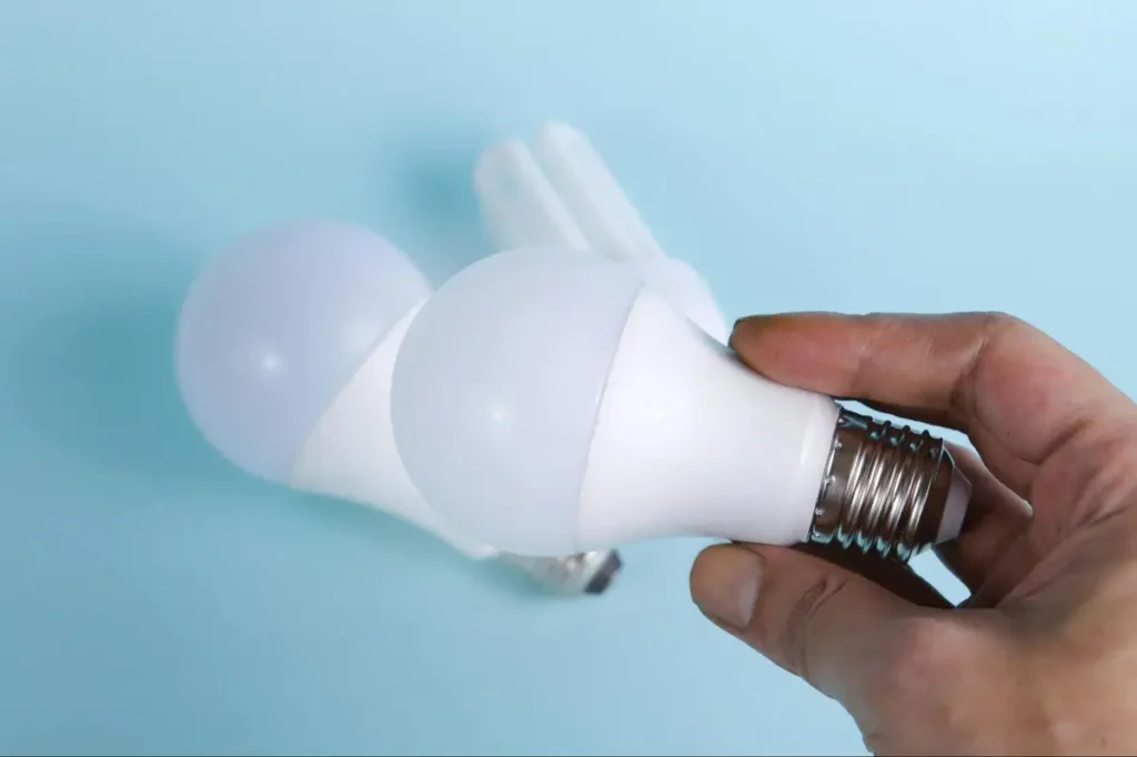 Hand holding LED light bulb against blue background, symbolizing innovative tech-themed events or sustainability conferences