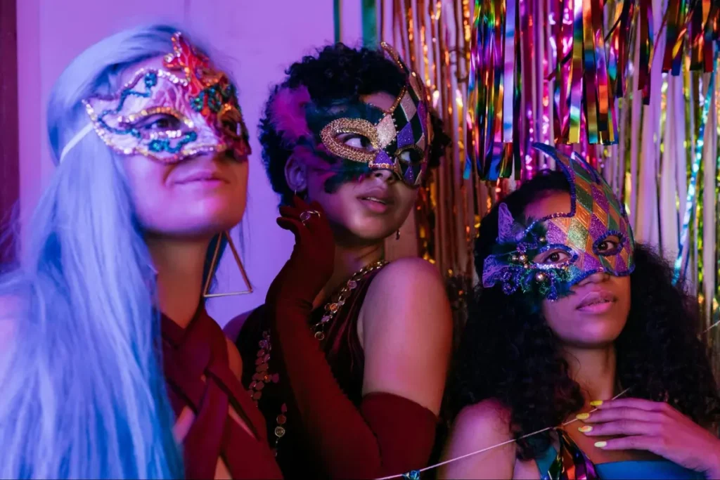 Masquerade ball event theme with three people wearing decorative face masks against colorful streamers background