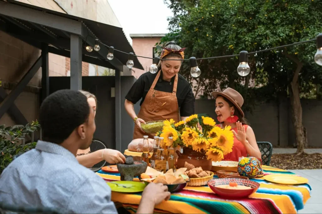 Mexican fiesta themed outdoor dining with sunflowers, colorful serape tablecloth, and guests enjoying authentic food
