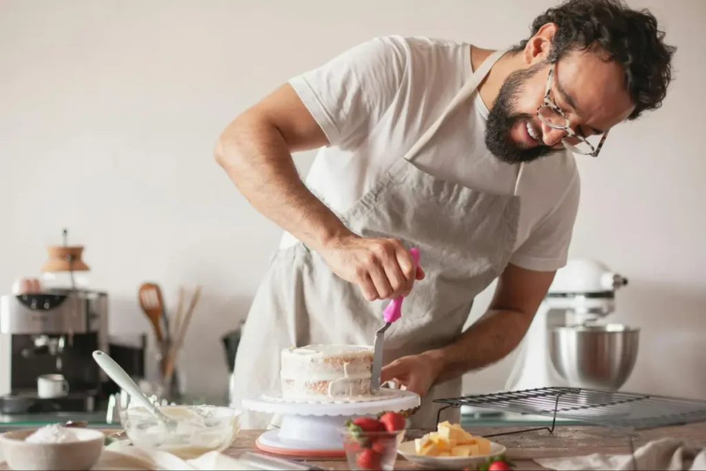 Person in white apron decorating a layered cake with pink spatula, perfect for baking-themed culinary events