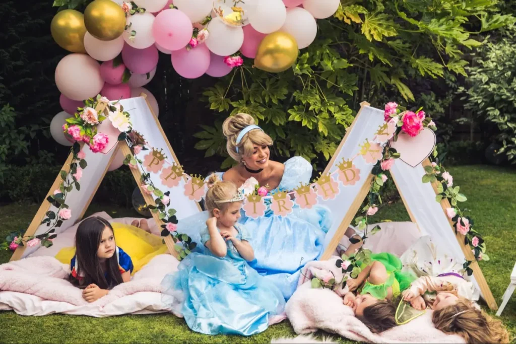 Princess-themed birthday party with a performer in blue dress entertaining children in a decorated tent with 'BIRTHDAY' banner