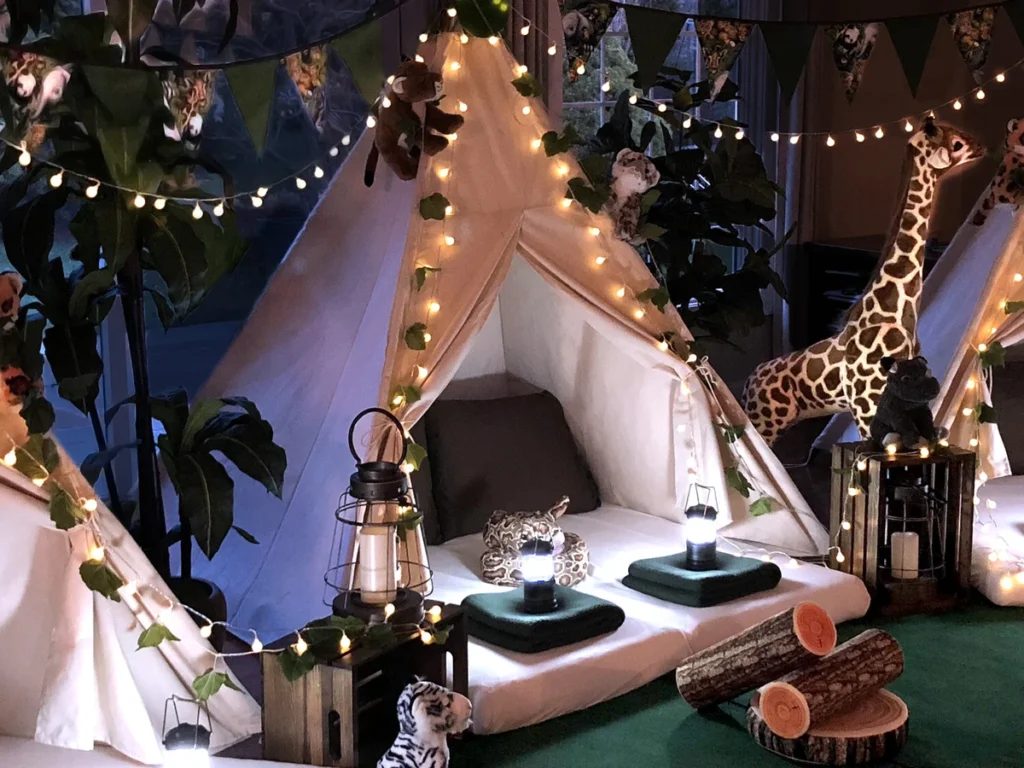 Safari-themed glamping setup with white teepee tents decorated with string lights, plush toys and lanterns for luxury outdoor events