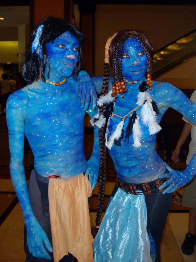 Two people in elaborate blue body paint and tribal accessories cosplaying as Avatar characters at themed convention