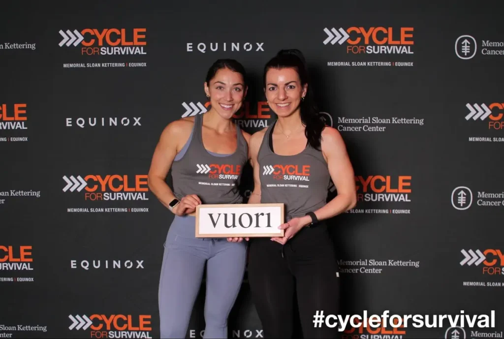 Two women in athletic wear holding sign at Cycle for Survival fundraiser - charity fitness event theme inspiration