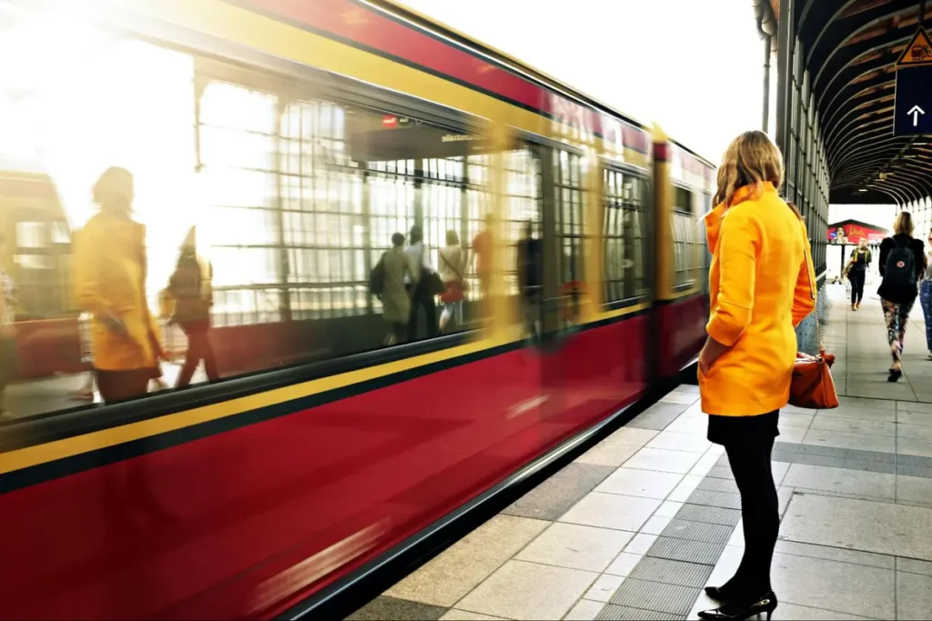 Woman in bright yellow coat waiting for train at urban transit station, perfect for commuter-themed corporate events