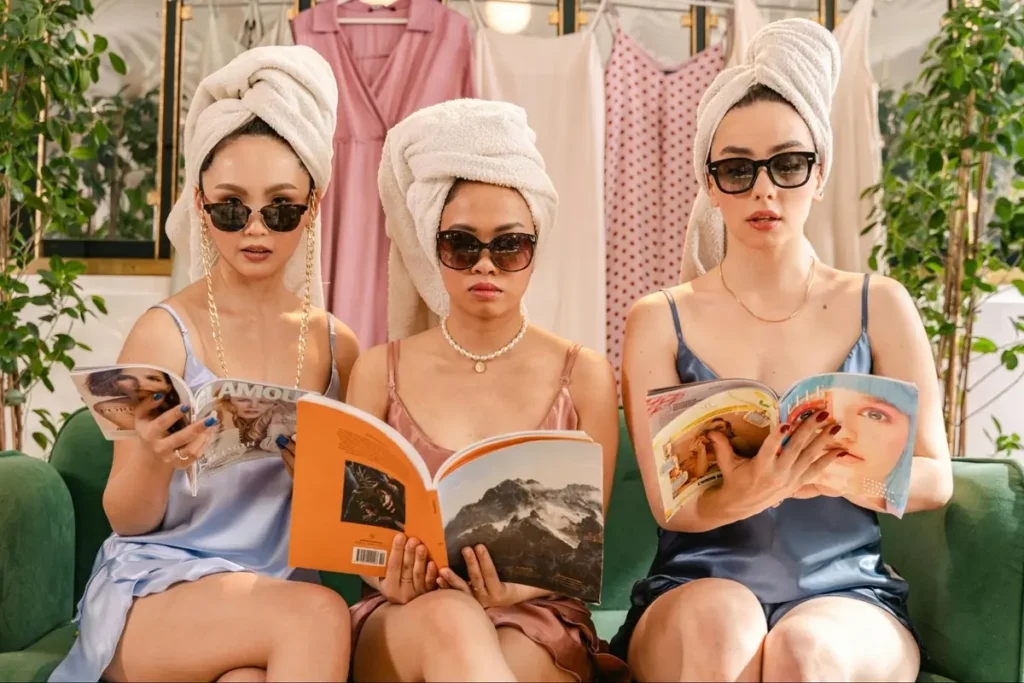 Women at spa-themed event with towel wraps and sunglasses reading magazines, ideal for wellness retreat gatherings